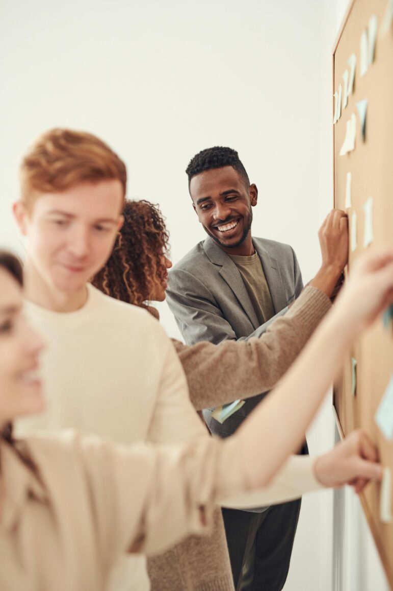 Guy smiling at others while pinning onto a corkboard.